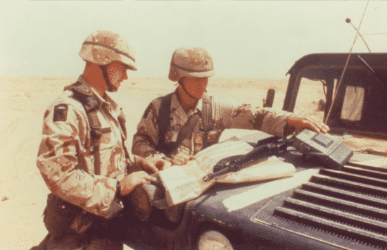 A photo of two soldiers in desert camouflage using a map on their vehicle (Courtesy of Department of War).
